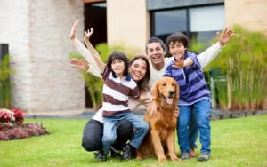 Padre, madre y dos hijos sonrientes con su perro en el jardín de su vivienda recién comprada en España