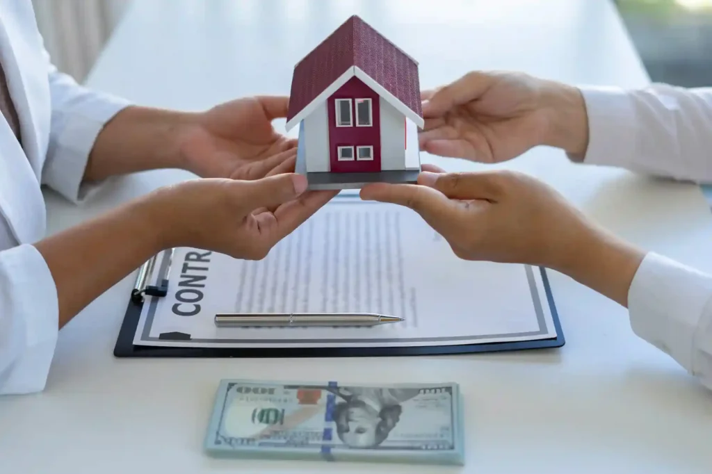 Manos sosteniendo una maqueta de casa sobre un contrato durante un proceso de compra de vivienda