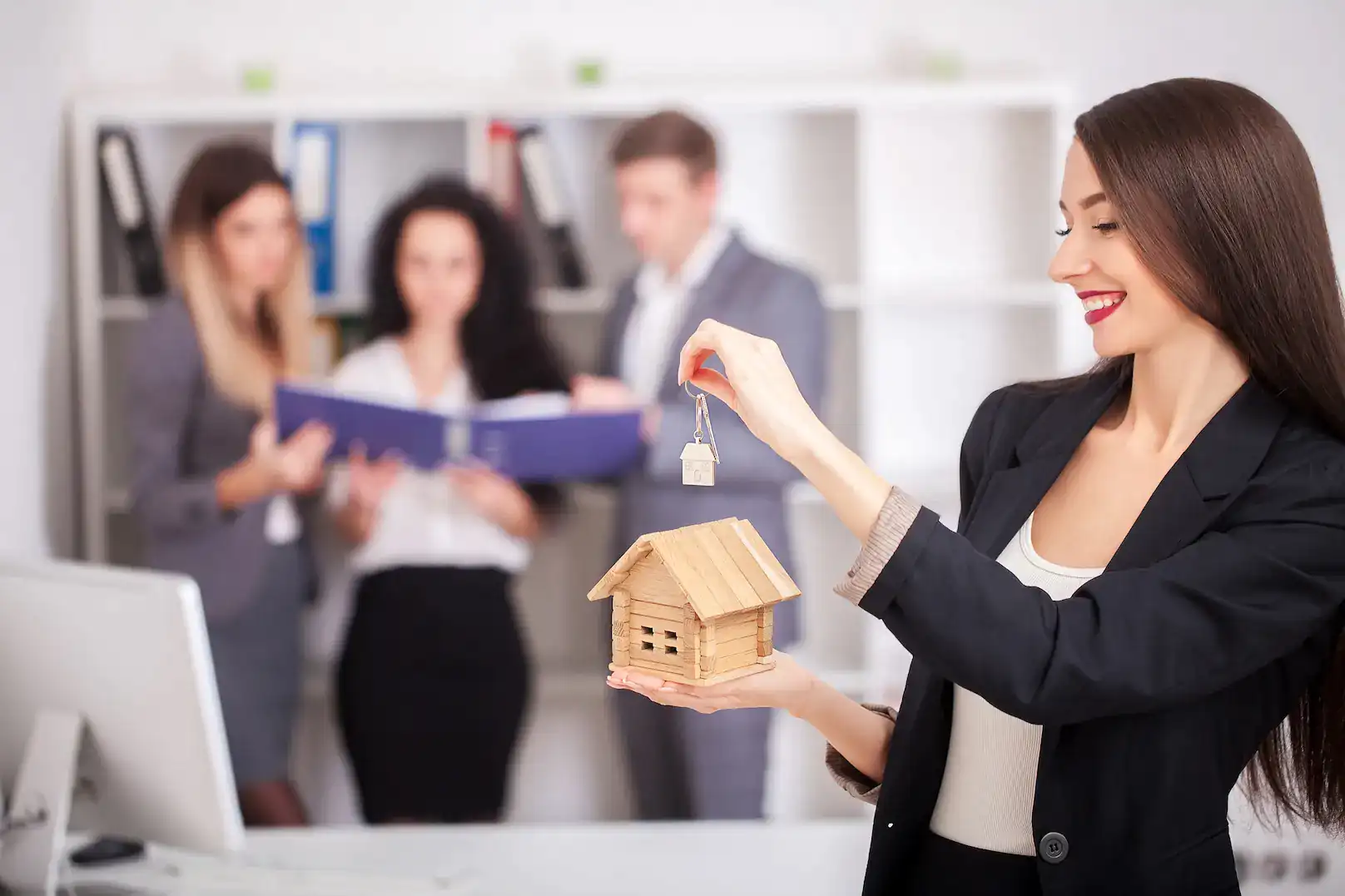 Asesora inmobiliaria sosteniendo una maqueta de casa y unas llaves durante una operación de compraventa