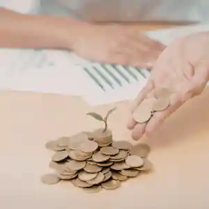 Monedas apiladas sobre una mesa mientras una persona sostiene varias monedas para representar una hipoteca al 100 sin ahorros