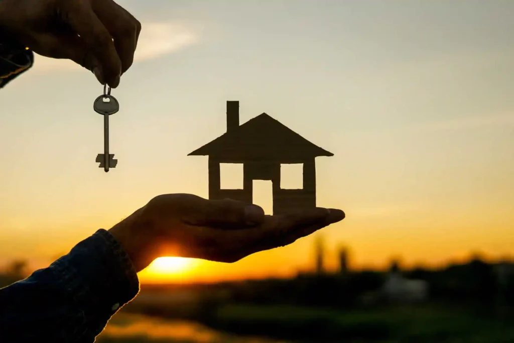 Mano entregando unas llaves junto a una casa para representar la compra de vivienda con hipoteca 95